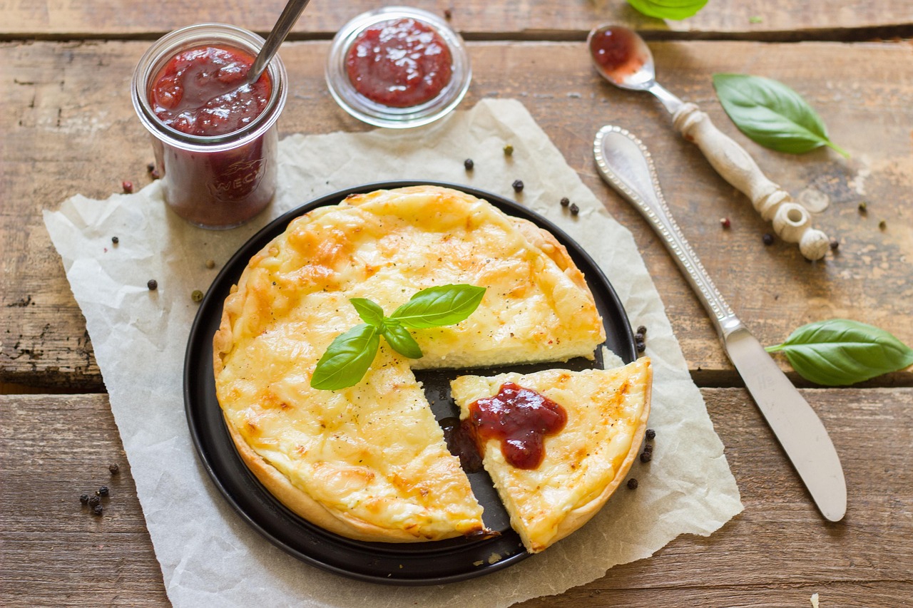 A golden cheese quiche on a dark plate with one slice cut and topped with chutney, on a wooden table