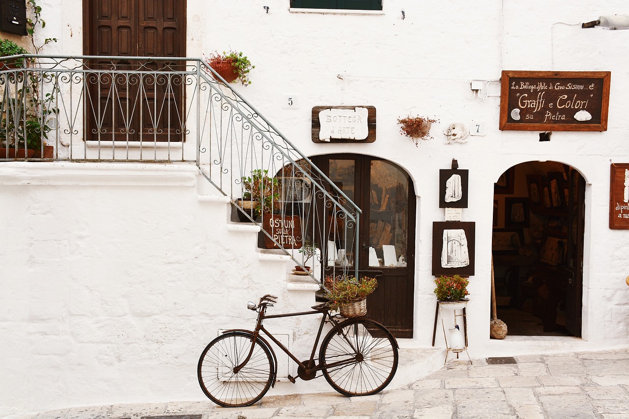 A whitewashed street with arched shop doorways, a wrought-iron stair rail and an old bicycle resting by the steps